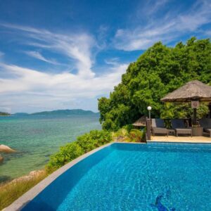 Pool terrace with thatched shades overlooking the sea and granite boulders at Chalets Cote Mer, Baie Ste Anne, Praslin