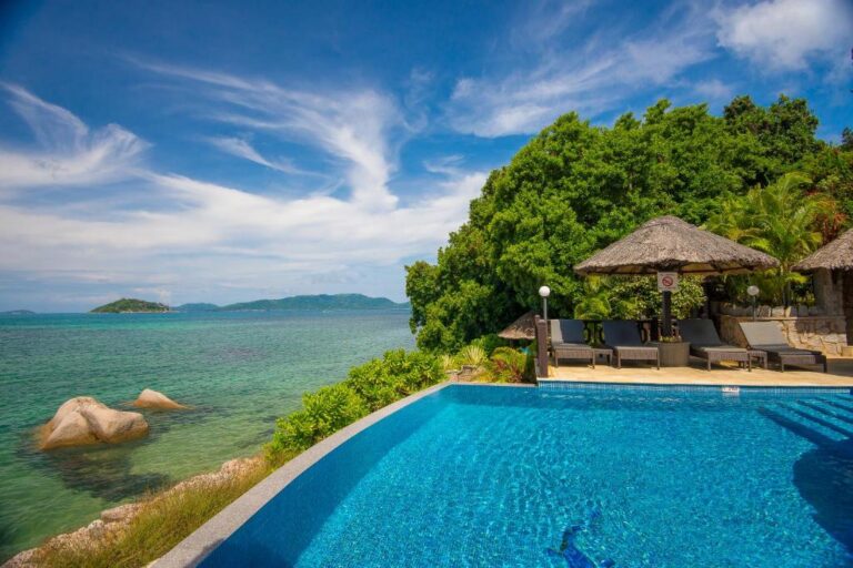 Pool terrace with thatched shades overlooking the sea and granite boulders at Chalets Cote Mer, Baie Ste Anne, Praslin