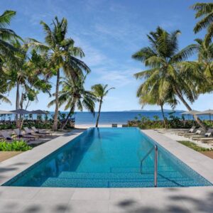 Outdoor pool with sun loungers and palm trees facing the sea at Indian Ocean Lodge, Grand Anse, Praslin