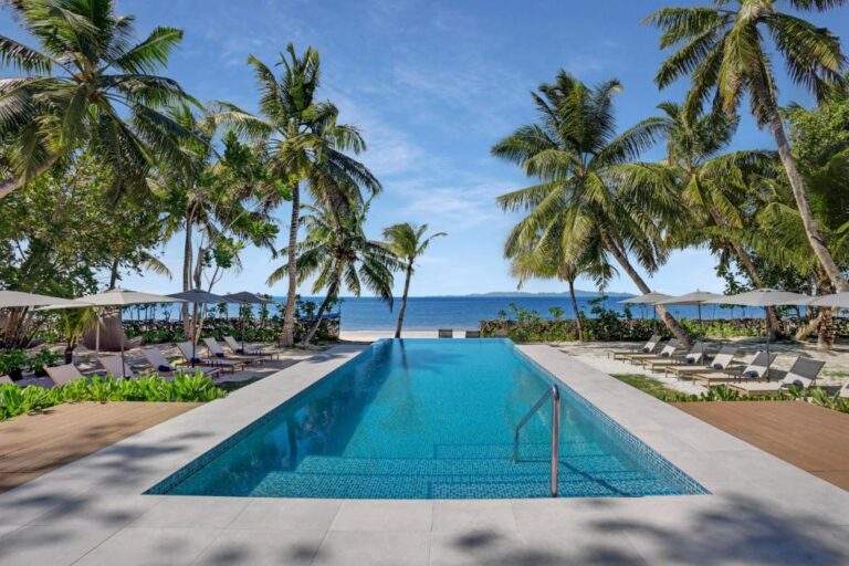Outdoor pool with sun loungers and palm trees facing the sea at Indian Ocean Lodge, Grand Anse, Praslin