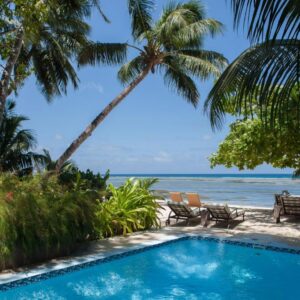 Pool and sun loungers under palm trees beside the beach at Le Repaire, Anse Réunion, La Digue